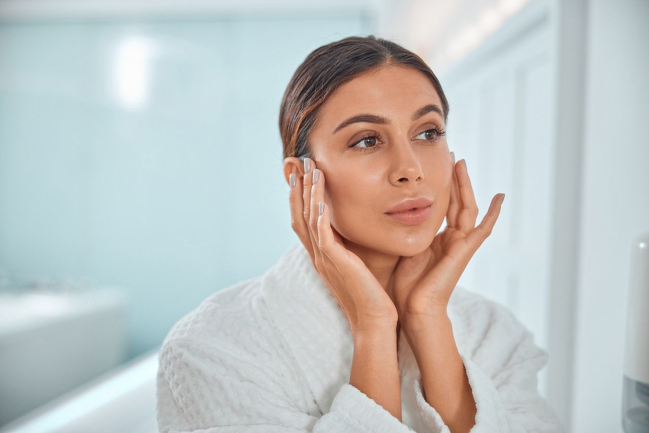 Woman applying skincare in a bathroom setting.
